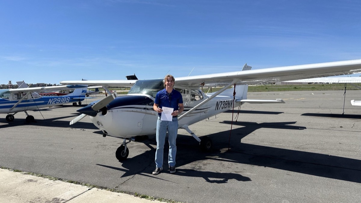 A student pilot standing beside a Cessna trainer on the ramp after a milestone flight